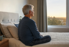 Älterer Mann sitzt am frühen Morgen am Bett und blickt aus dem Fenster [Bildinhalt mit KI erstellt]